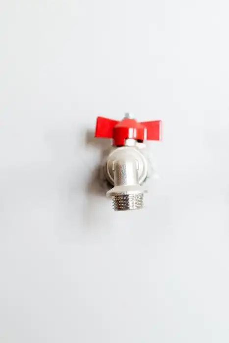 Two metal faucets with red handles are mounted on a white wall.